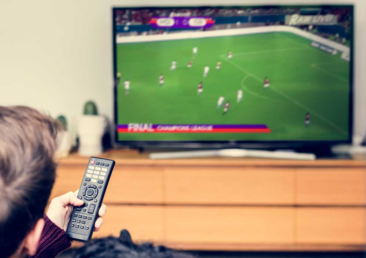A person watching a football match on their TV and checking live betting odds, illustrating a guide to in-play betting.
