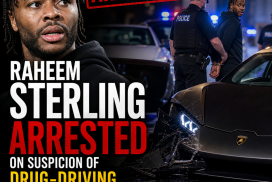 Raheem Sterling being led by police officers wearing handcuffs outside a building.